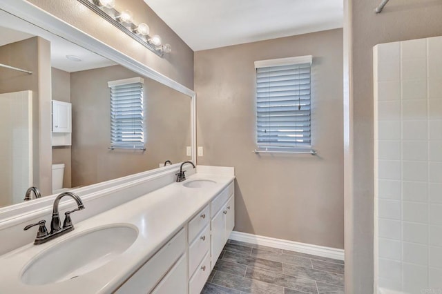 bathroom featuring toilet, a sink, baseboards, and double vanity