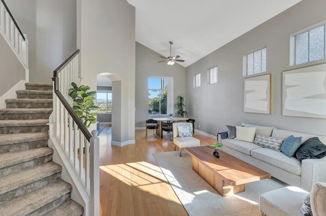 living room featuring arched walkways, high vaulted ceiling, light wood-style flooring, baseboards, and stairs