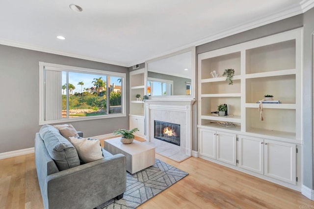 living area with light wood finished floors, a tiled fireplace, baseboards, and crown molding