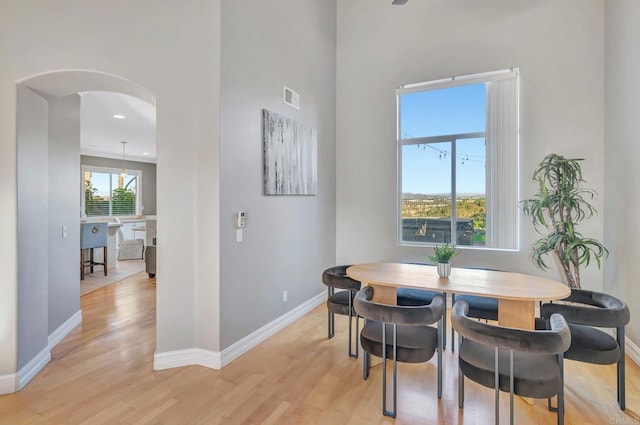 dining space featuring light wood-style flooring, visible vents, arched walkways, and baseboards