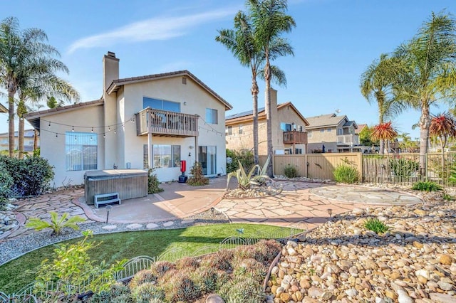 rear view of property with a chimney, a hot tub, a patio area, fence, and a balcony