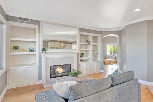 living room with baseboards, visible vents, arched walkways, built in features, and a tile fireplace