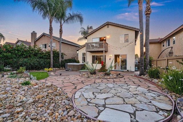 back of property featuring a balcony, fence, stucco siding, a patio area, and a hot tub