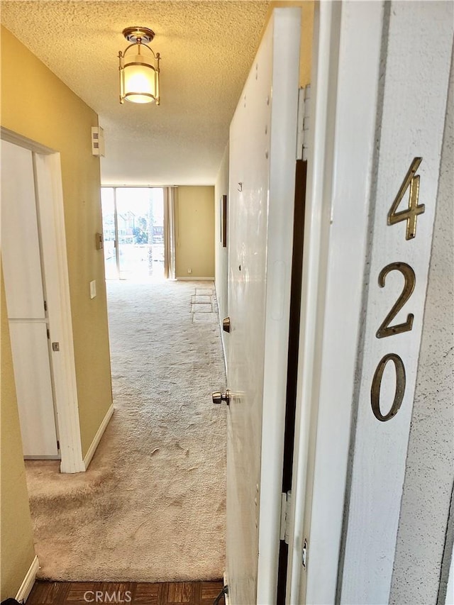 corridor with a textured ceiling, carpet floors, and baseboards