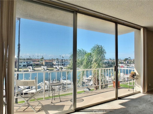 doorway to outside with a water view, expansive windows, carpet floors, and a textured ceiling