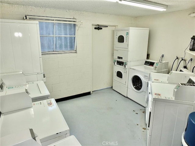 common laundry area featuring a textured ceiling, independent washer and dryer, stacked washer and clothes dryer, and concrete block wall