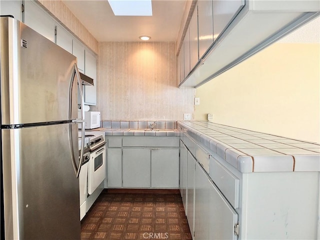 kitchen featuring tile countertops, high quality stove, a skylight, and freestanding refrigerator