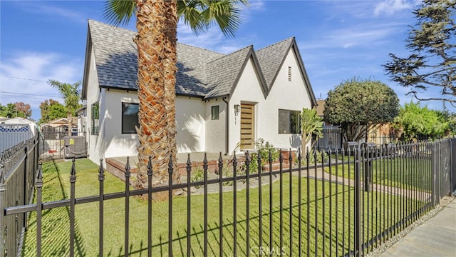 tudor home with fence private yard, a shingled roof, a front lawn, and stucco siding