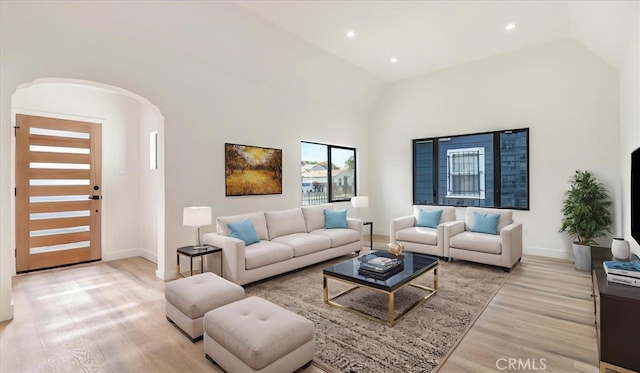 living room featuring arched walkways, recessed lighting, light wood-style flooring, high vaulted ceiling, and baseboards