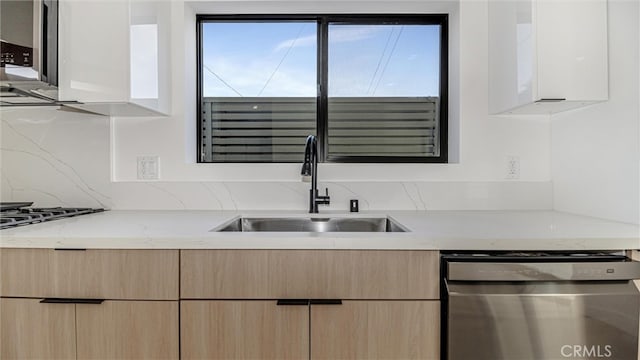 kitchen featuring light brown cabinetry, stainless steel dishwasher, modern cabinets, and a sink