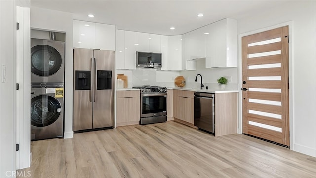 kitchen featuring stainless steel appliances, stacked washer / drying machine, light countertops, white cabinetry, and modern cabinets