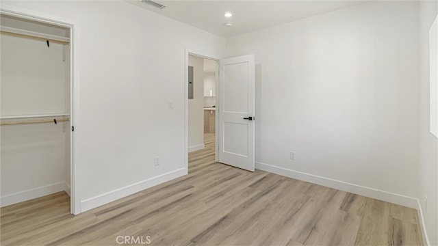 unfurnished bedroom featuring light wood-style flooring, visible vents, baseboards, a closet, and electric panel