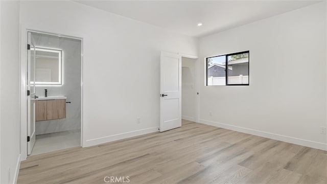 unfurnished bedroom featuring light wood-type flooring, ensuite bathroom, baseboards, and recessed lighting