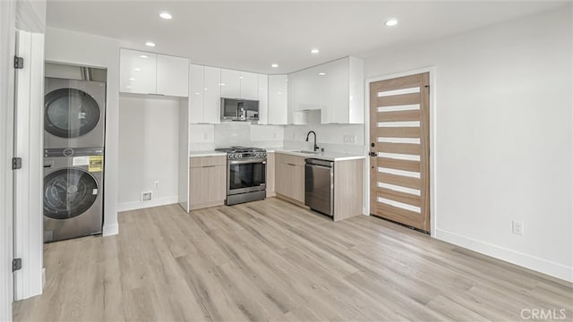 kitchen featuring a sink, white cabinetry, light countertops, appliances with stainless steel finishes, and stacked washer and clothes dryer