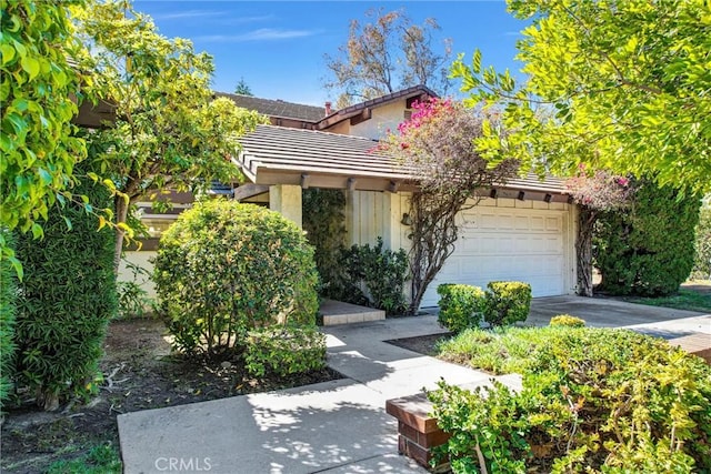 obstructed view of property with a garage, a tile roof, concrete driveway, and stucco siding