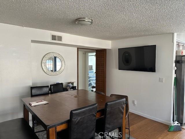 dining area with visible vents, a textured ceiling, baseboards, and wood finished floors