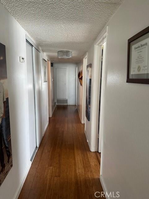 corridor featuring a textured ceiling, baseboards, and dark wood-type flooring