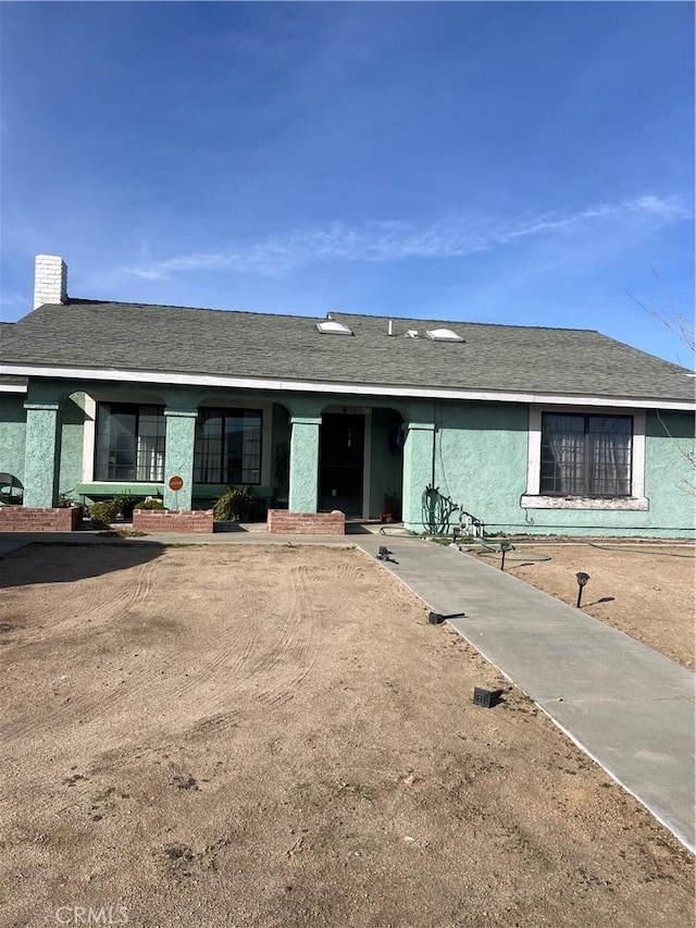 ranch-style house with a shingled roof, a chimney, and stucco siding