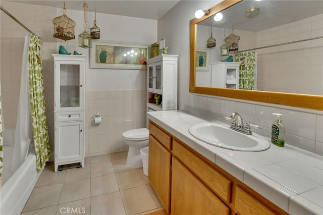 bathroom featuring toilet, tile patterned floors, shower / bath combo with shower curtain, vanity, and tile walls