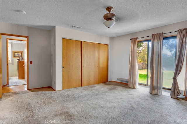 unfurnished bedroom featuring a textured ceiling, light colored carpet, visible vents, access to outside, and a closet