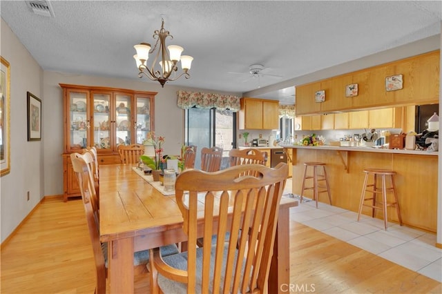 dining area featuring light wood finished floors, visible vents, a textured ceiling, and ceiling fan with notable chandelier