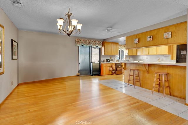 kitchen with decorative light fixtures, a breakfast bar area, light countertops, visible vents, and a peninsula