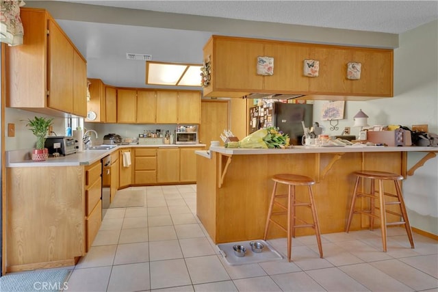 kitchen with a kitchen breakfast bar, a peninsula, light countertops, light brown cabinetry, and light tile patterned flooring