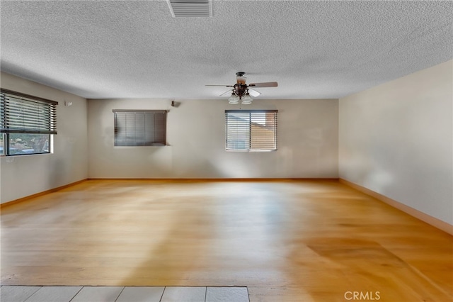 unfurnished room with visible vents, light wood-style flooring, ceiling fan, a textured ceiling, and baseboards