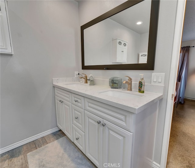 full bath featuring double vanity, wood finished floors, a sink, and baseboards