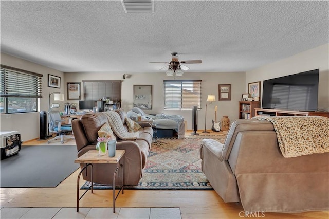 living room with a textured ceiling, light wood-type flooring, visible vents, and a ceiling fan