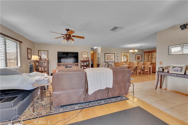 living room with a textured ceiling, light tile patterned floors, ceiling fan with notable chandelier, visible vents, and baseboards