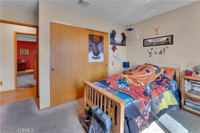 carpeted bedroom with a closet, visible vents, and a textured ceiling