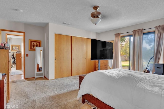 bedroom with a closet, light colored carpet, visible vents, a textured ceiling, and baseboards