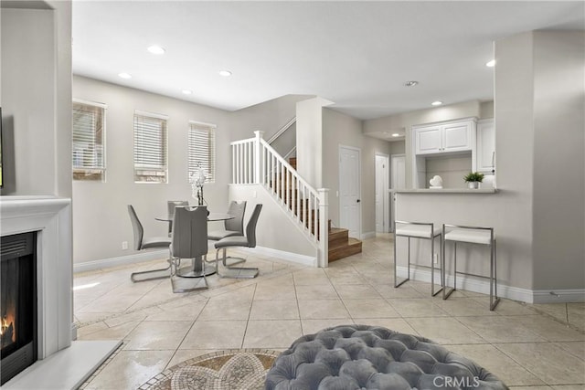 dining space with light tile patterned floors, baseboards, a glass covered fireplace, stairway, and recessed lighting