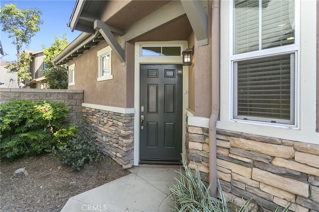 doorway to property featuring stone siding, fence, and stucco siding