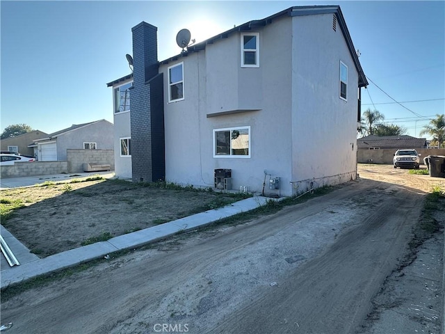 back of house with a chimney, fence, and stucco siding