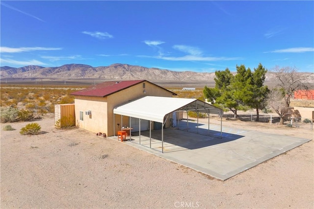 view of outdoor structure featuring concrete driveway, a carport, fence, and a mountain view