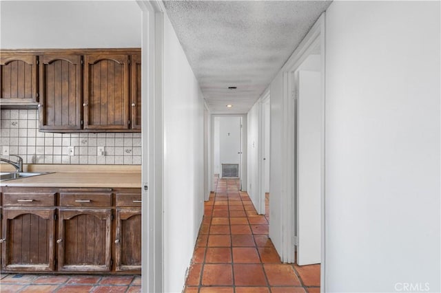 hall with dark tile patterned flooring, visible vents, a sink, and a textured ceiling