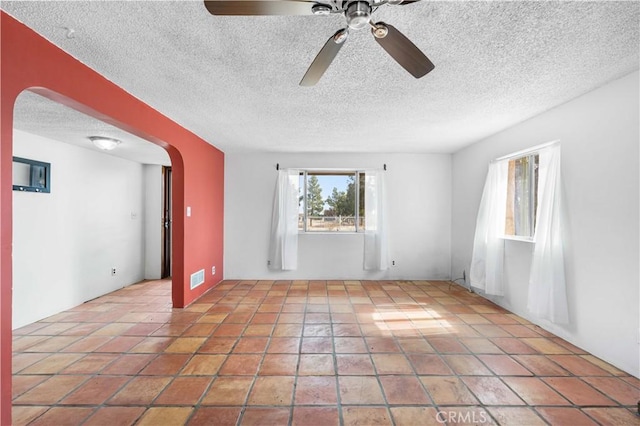 tiled spare room with arched walkways, visible vents, and a textured ceiling