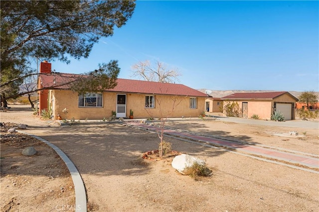 ranch-style home with a garage, driveway, a chimney, and stucco siding