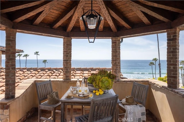 balcony with a water view, a beach view, and outdoor dining area