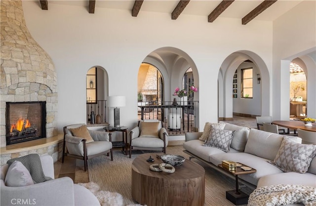 living area with arched walkways, an outdoor stone fireplace, beamed ceiling, and a towering ceiling