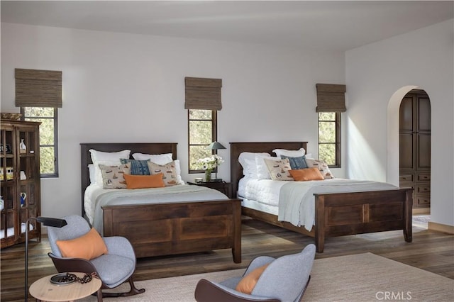 bedroom featuring arched walkways, multiple windows, and dark wood finished floors