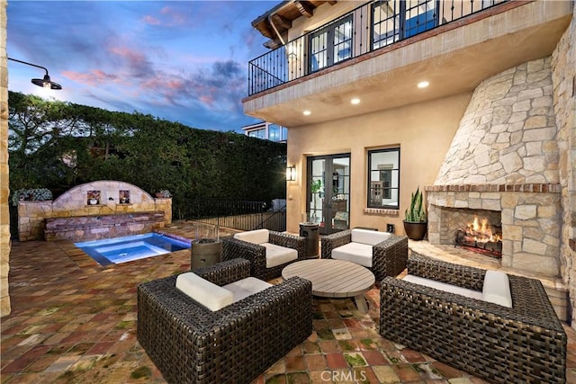 patio terrace at dusk featuring an outdoor living space with a fireplace, fence, and an in ground hot tub