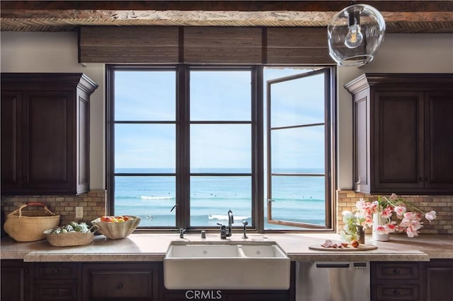 kitchen with dark brown cabinetry, a water view, a sink, and stainless steel dishwasher