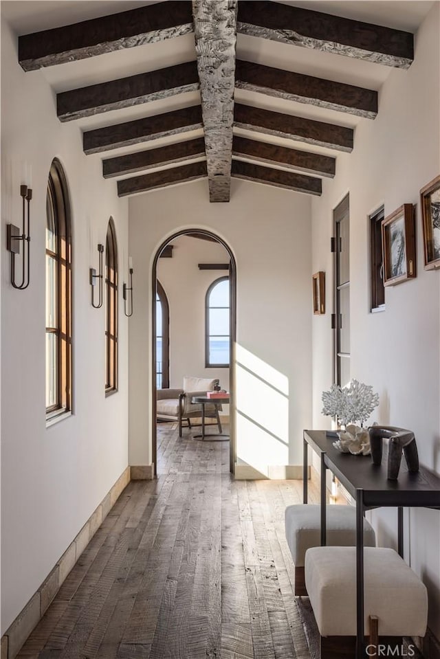 corridor featuring arched walkways, wood finished floors, beam ceiling, and baseboards