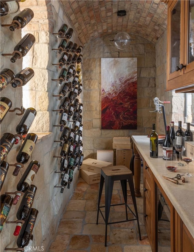 wine cellar featuring brick ceiling, stone tile flooring, vaulted ceiling, and wine cooler