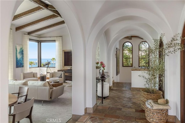 hall with vaulted ceiling with beams, a water view, arched walkways, and stone tile floors