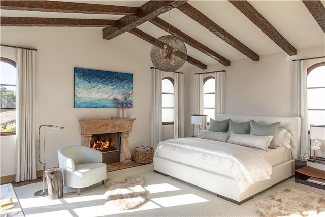 bedroom with multiple windows, vaulted ceiling with beams, and a lit fireplace