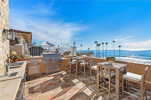 view of patio with a water view, a grill, a beach view, and a sink